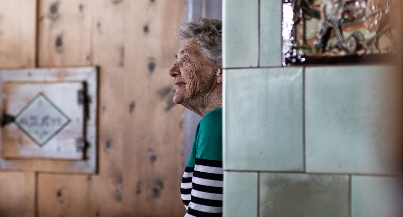 Alte Fisserin sitzt auf ihrer Ofenbank in einer Bauernstube in Serfaus-Fiss-Ladis in Tirol | © Serfaus-Fiss-Ladis Marketing GmbH | Rene Raggl