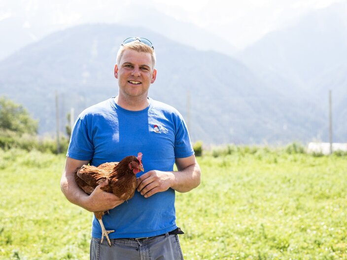 Florian Plangger von den Fisser Goggala mit einem Huhn auf dem Arm Bauernläden in Serfaus-Fiss-Ladis in Tirol | © Serfaus-Fiss-Ladis Marketing GmbH | Rene Raggl