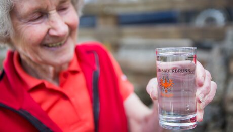 Seniorchefin Burgl mit einem Glas frischem Sauerbrunn aus Ladis in Tirol | © Socialweb