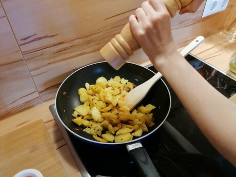 Für das Tiroler Gröstl aus Serfaus-Fiss-Ladis müssen die Kartoffelscheiben in die Pfanne gegeben und gewürzt werden | © Serfaus-Fiss-Ladis