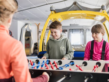 Kinder im Skiurs beim Tischfußballspielen im Kinderrestaurant Starrest Blogbeitrag | © Serfaus-Fiss-Ladis Marketing GmbH | Fabian Schirgi