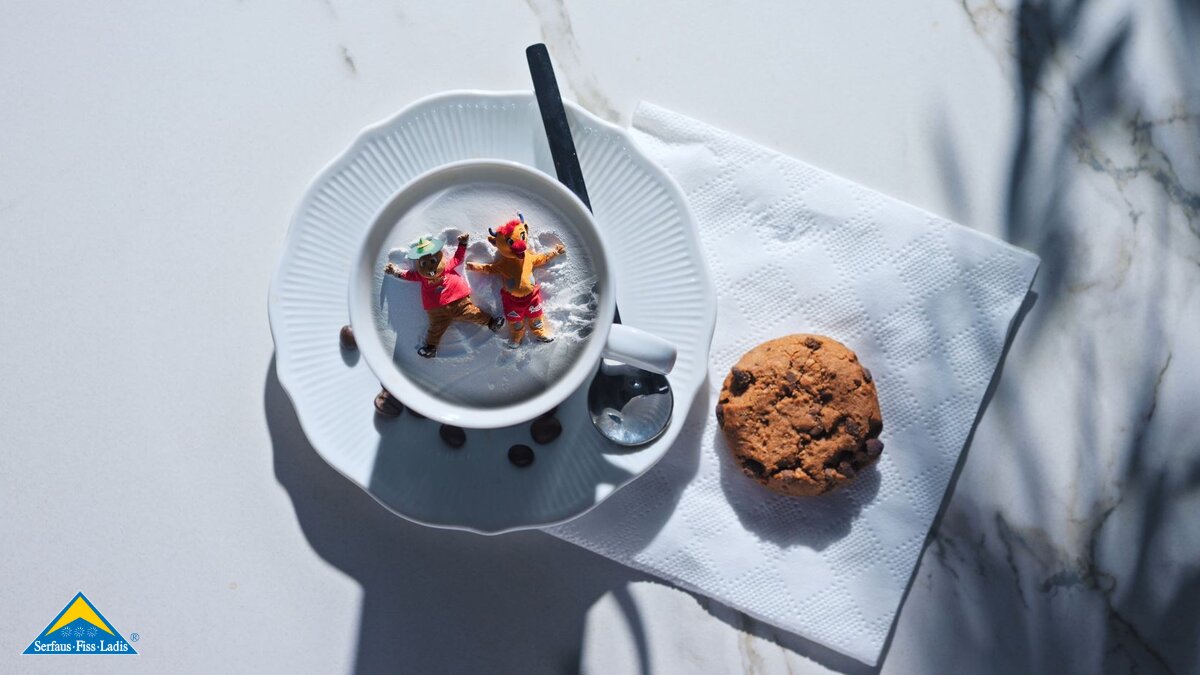 Maskottchen Murmli und Berta machen einen Schneeengel Kaffeetasse Familienregion Serfaus-Fiss-Ladis in Tirol | © Serfaus-Fiss-Ladis Marketing GmbH | Mattias Nigg Films