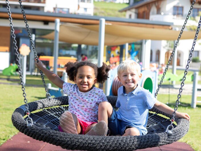 Schaukelnde Kinder im Spielplatz Kulturhaus Fiss Kinderclub Mini&Maxi Club in der Familienregion Serfaus-Fiss-Ladis in Tirol | © Serfaus-Fiss-Ladis Marketing GmbH | Andreas Kirschner