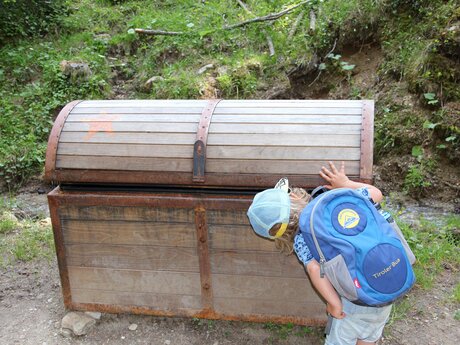 Kind blickt in Schatztruhe aus Holz auf dem Piratenweg in Serfaus-Fiss-Ladis Blog Abenteuerberge | © Serfaus-Fiss-Ladis Marketing GmbH