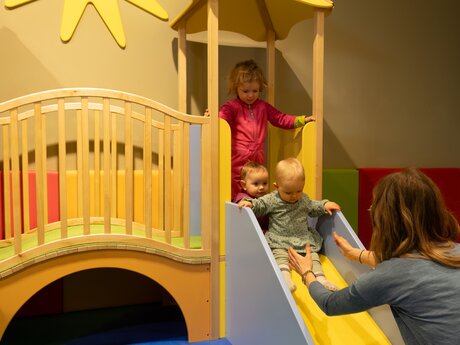Kleinkind rutscht mit Hife von Mutter Softplayanlage indoor Spielplatz Winterurlaub Serfaus-Fiss-Ladis Blogbeitrag Tirol | © Serfaus-Fiss-Ladis Marketing GmbH | Andreas Kirschner