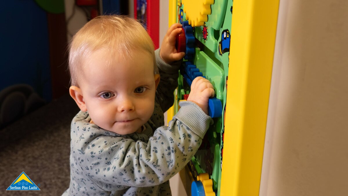 indoor Spielplatz Kleinkind steht an der Wand und spielt an einer interaktiven Spielestation Alternative zum Skifahren Serfaus-Fiss-Ladis in Tirol | © Serfaus-Fiss-Ladis Marketing GmbH | Andreas Kirschner